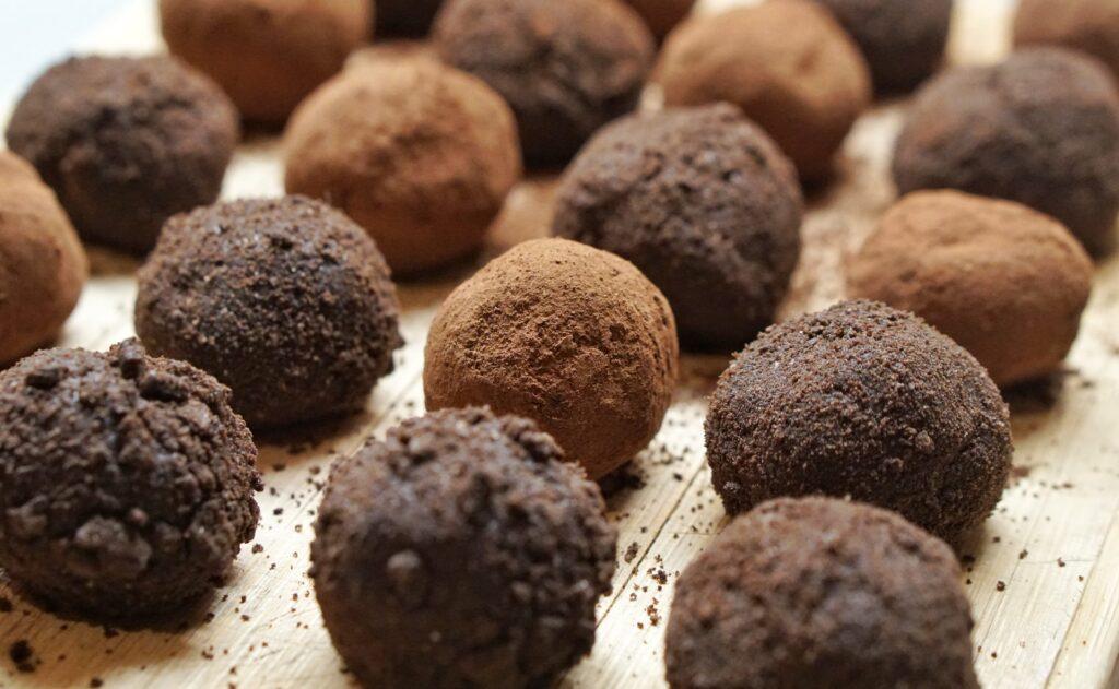 Chocolate truffles laid out on a wooden table. Dark and light brown coloured circular chocolate is lined up in rows.