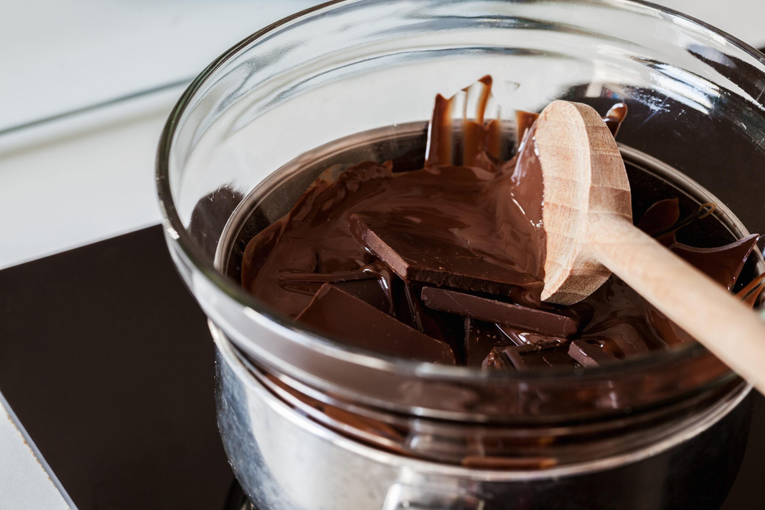 Melting Chocolate in glass container is mixed with a wooden spatula.