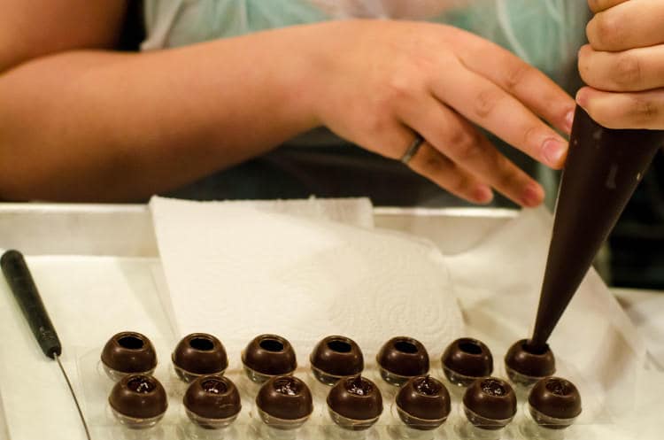 Hands rolling chocolate truffles during a truffle-making workshop at Chocolatetales, with bowls of melted chocolate and cocoa powder on the table